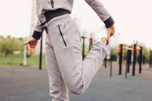 Atractiva en forma de mujer joven en el deporte gris llevar el calentamiento haciendo estiramiento antes de entrenar en la calle área de entrenamiento. El estilo de vida saludable en la ciudad —  Fotos de Stock