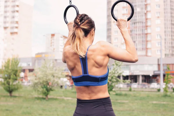 Attractive fit young woman in sport wear girl pulls up on the rings at street workout area. The healthy lifestyle in city — Stock Photo, Image