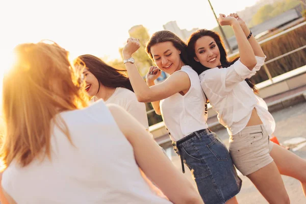 Группа красивых беззаботных девушек танцует весело на городской парковке на фоне вечернего заката, летнего времени — стоковое фото