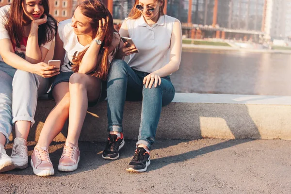 Three young happy girls real friends students using mobile at city street on sunset background — Stock Photo, Image