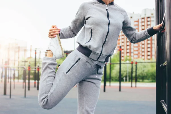 Atractiva mujer joven en forma de deporte gris llevar el calentamiento haciendo estiramiento antes de entrenar en el área de entrenamiento de la calle. El estilo de vida saludable en la ciudad — Foto de Stock