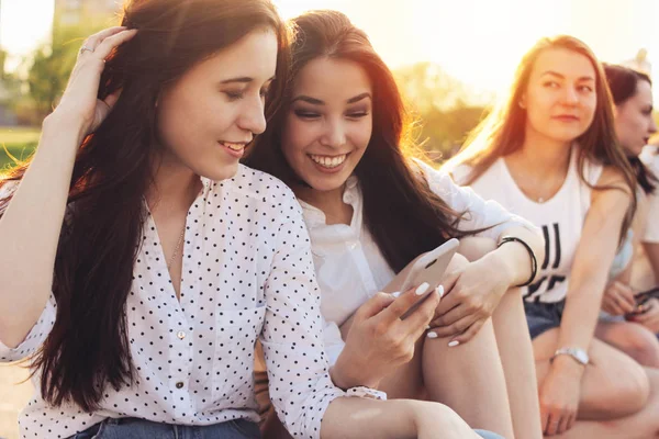 Grupo de jovens meninas felizes amigos reais estudantes usando móvel na rua da cidade no pôr do sol fundo — Fotografia de Stock