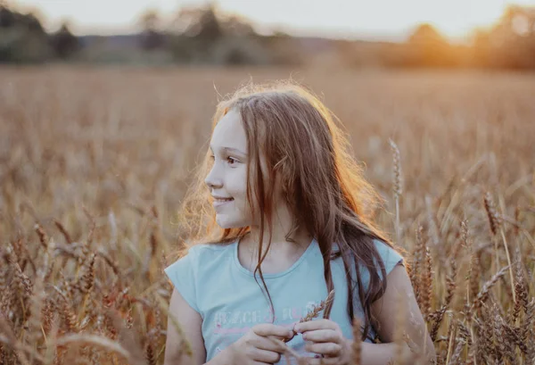 Feliz linda tweens menina com cabelos longos no campo de trigo ao pôr do sol — Fotografia de Stock