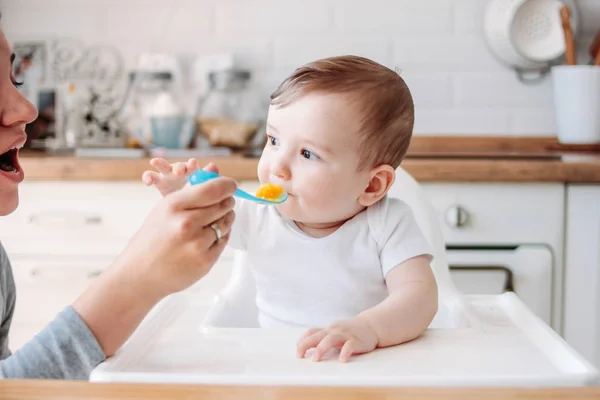 Encantador menino 6-8 meses comendo a primeira abóbora de comida da colher com a mãe em casa — Fotografia de Stock