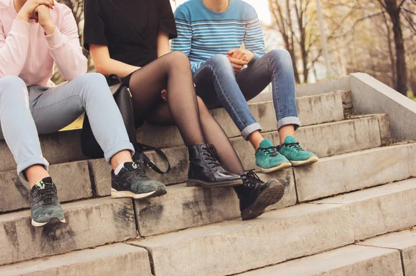 Oříznout fotografii skupiny přátel tisíciletí studentů, kteří sedí na ulici, přátelství, zblízka zaostření na nohy — Stock fotografie