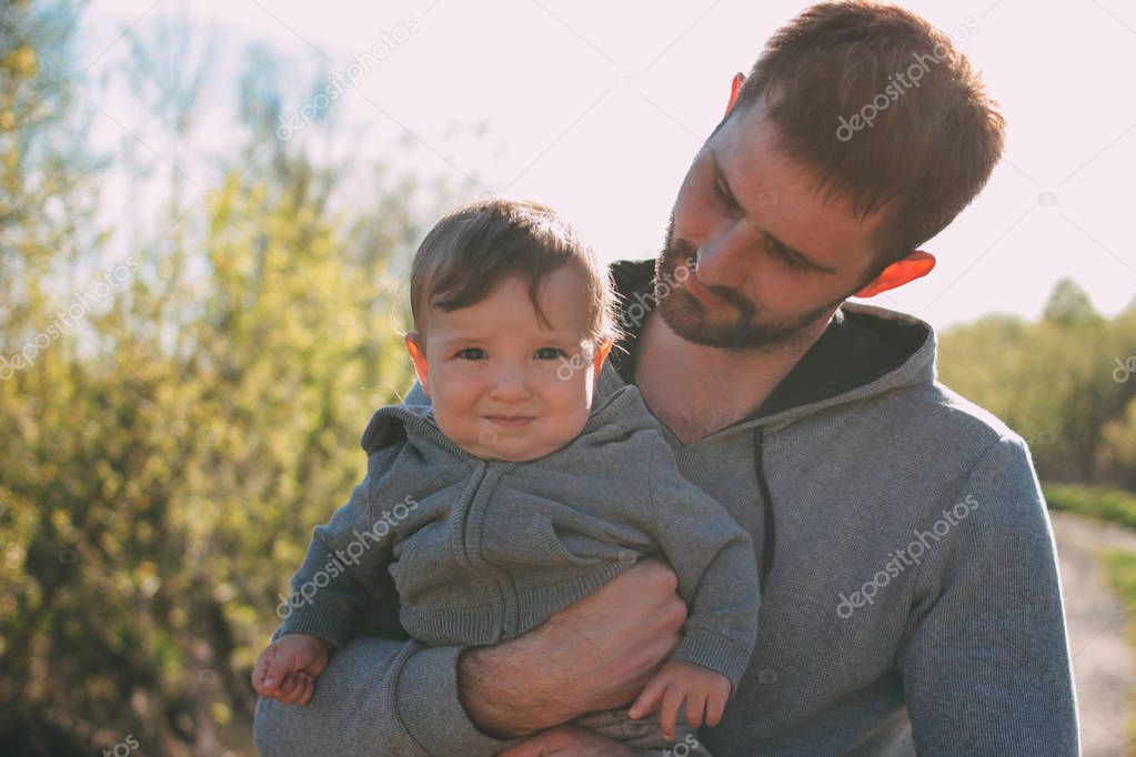 Cute baby boy on his dad's shoulders walking on road outdoors, sensitivity to nature concept