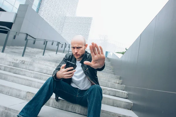 Adulto careca barbudo homem sério com móvel sentado na escada fechando câmera à mão, não mais foto — Fotografia de Stock