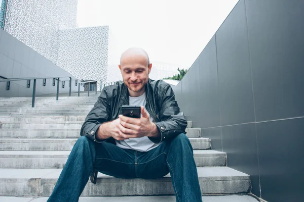 Adulto careca barbudo homem usando móvel e sentado na escada na rua da cidade — Fotografia de Stock