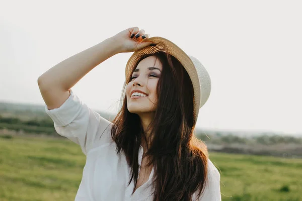 Mooie zorgeloze lang haar Aziatisch meisje in witte kleren en strohoed geniet van het leven in de natuurgebied bij zonsondergang. Gevoeligheid voor natuur concept — Stockfoto