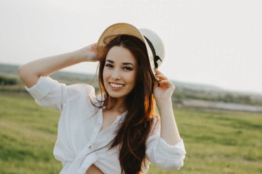 Beyaz giysiler ve saman şapka güzel kaygısız uzun saçlı Asya Kız portresi gün batımı doğa alanında yaşam sahiptir. Doğa konseptine duyarlılık