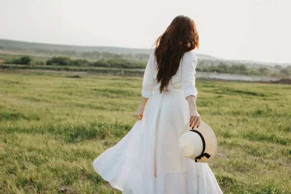 Bella ragazza spensierata capelli lunghi in vestiti bianchi e cappello di paglia gode la vita in campo naturale al tramonto. Sensibilità al concetto di natura — Foto Stock