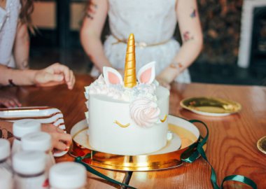 Çocukların elleri küçük kızlar pastaya uzanır. Şenlikli masada küçük Prenses doğum gününde Büyük güzel pasta tek boynuzlu at