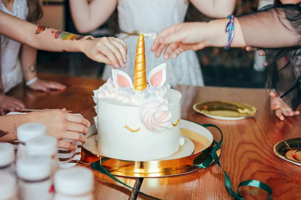 Children's hands little girls reach for the cake. Big beautiful cake unicorn on birthday of little Princess on festive table