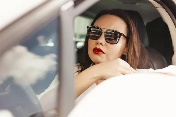 Mooie succesvolle elegante brunette jonge vrouw met rode lippen in zonnebril rijden personenauto — Stockfoto