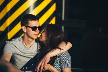 Gündelik tarzda giyinmiş genç aşıklar şehir sokaklarında yan yana oturuyorlar.