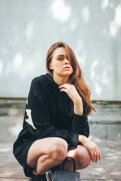 Candid portrait of young beautiful long hair girl fashion model hipster in black hoodie on wall background