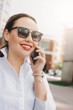 Şehir caddesinde mobil kullanarak güneş gözlüğü esmer zarif kadın iş kadını yakın portresi