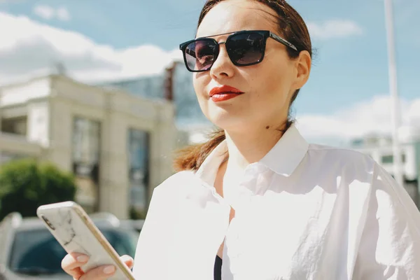 Крупный план портрет брюнетки элегантной женщины бизнес-леди в солнечных очках с помощью мобильного телефона на городской улице — стоковое фото