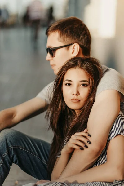 Jovem casal feliz no amor adolescentes amigos vestidos em estilo casual sentados juntos na rua da cidade. Menina asiática bonita, pessoas multirraciais — Fotografia de Stock