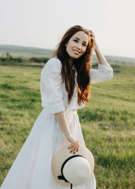 Beyaz giysiler ve hasır şapka güzel kaygısız uzun saçlı asya kız gün batımında alanında yaşam sahiptir. Doğa kavramına duyarlılık