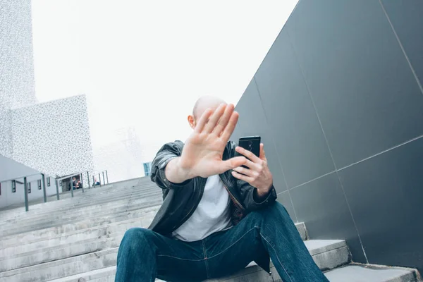 Adulto careca barbudo homem sério com móvel sentado na escada fechando câmera à mão, não mais foto — Fotografia de Stock