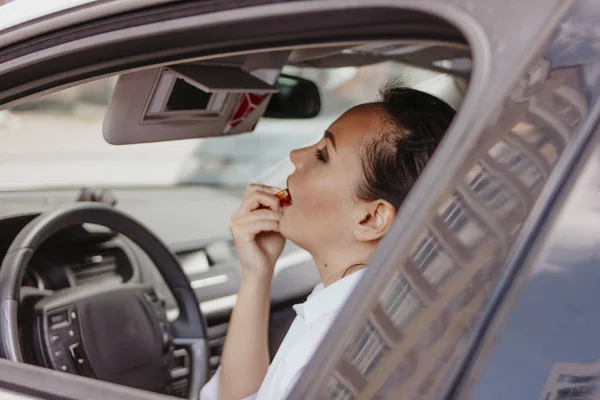 Mooie succesvolle elegante brunette jonge vrouw die haar lippen met rode Lipstick in de auto schilderij — Stockfoto