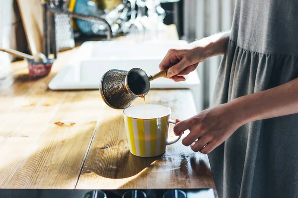 Молодая женщина наливает натуральный свежий кофе в кружку на кухне, утром, жесткий свет — стоковое фото