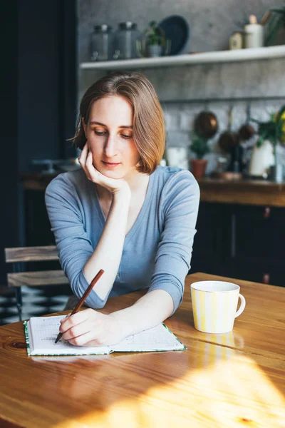 Young woman southpaw lefthender calculates family budget, writes in diary in the kitchen — Stock Photo, Image