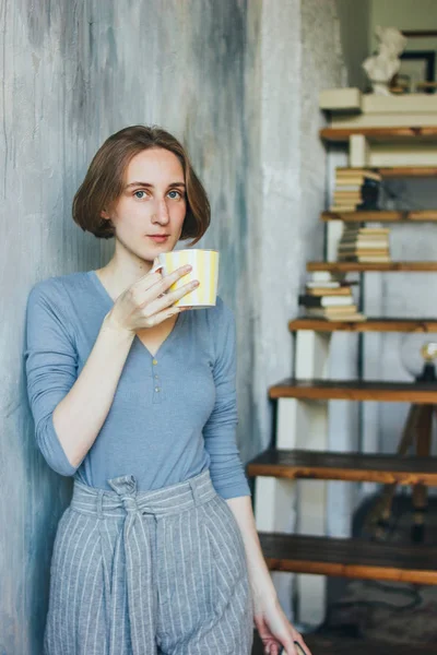 Jovem mulher com copo amarelo em pé contra a parede no estúdio de arte, retrato vertical — Fotografia de Stock