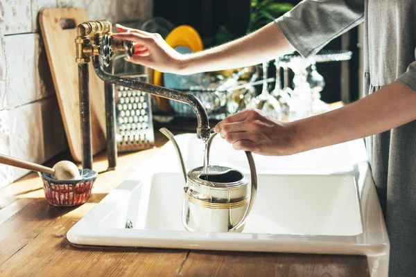 Молодая женщина в сером платье наливает воду в чайник на кухне, утренняя рутина — стоковое фото