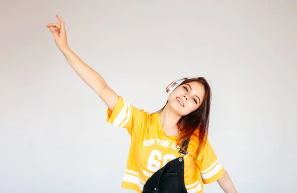 Heureuse adolescente souriante insouciante aux cheveux longs foncés en t-shirt jaune écoutant de la musique dans des écouteurs isolés sur fond gris — Photo