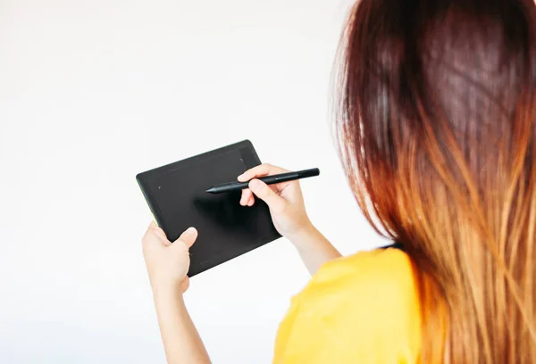 Graphic tablet with pen in hands of young woman in yellow t-shirt, isolated on grey background