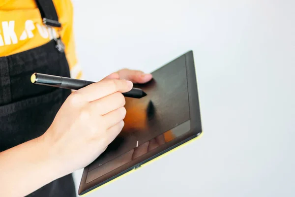 Comprimido gráfico com caneta nas mãos de mulher jovem em camiseta amarela, isolado sobre fundo cinzento — Fotografia de Stock