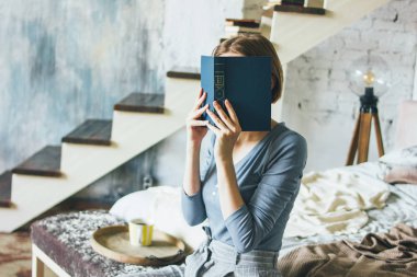 Genç kadın yakın yüz kitap loft sanat eseri stüdyo odasında yatakta oturan