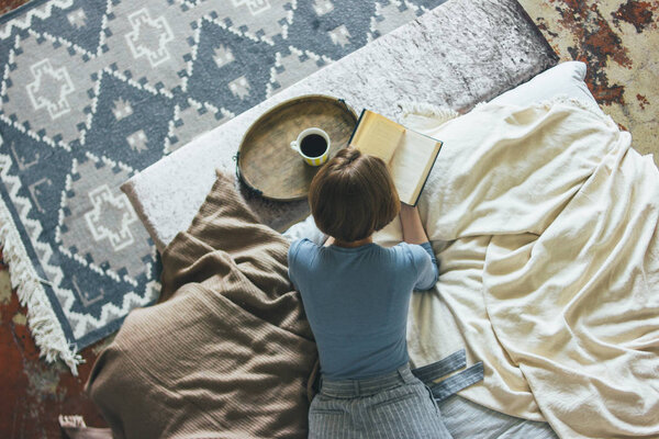 Young woman reading book on bed in loft room, slow life