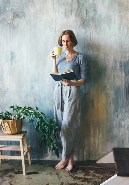 노란 컵을 벽에 대고 서있는 젊은 여성, 아트 워크 스튜디오에서 책을 읽고, 수직 초상화 — 스톡 사진