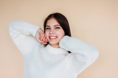 Bej arka planda rahat beyaz kazak temiz cilt ve koyu uzun saçlı güzel gülümseyen kız