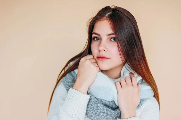 Bella ragazza con pelle pulita e capelli lunghi scuri in accogliente maglione bianco e sciarpa calda su sfondo beige — Foto Stock