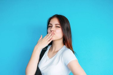 Beyaz t-shirt koyu uzun saçlı güzel kaygısız gülümseyen kız mavi arka planda izole hava öpücük yapma