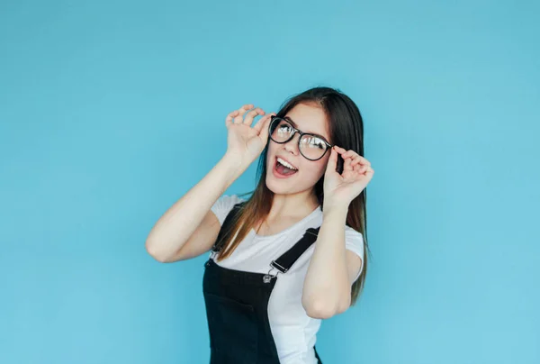 Menina feliz bonita em óculos com cabelos longos escuros em t-shirt branca isolada no fundo azul — Fotografia de Stock