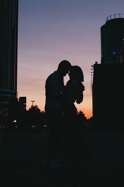 Silhueta de jovem casal feliz no amor beijando na rua da cidade ao pôr do sol — Fotografia de Stock