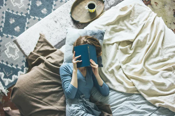 Молода жінка читає книгу на ліжку в кімнаті лофт, повільне життя — стокове фото