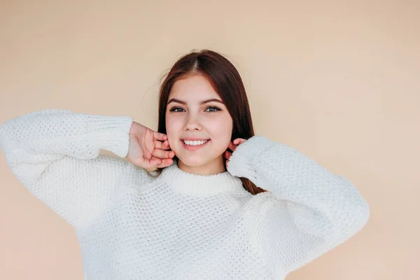 Bella ragazza sorridente con pelle pulita e capelli lunghi scuri in accogliente maglione bianco su sfondo beige — Foto Stock