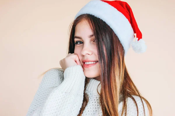Menina sorridente bonita com pele limpa em santa hat um suéter branco acolhedor no fundo bege — Fotografia de Stock