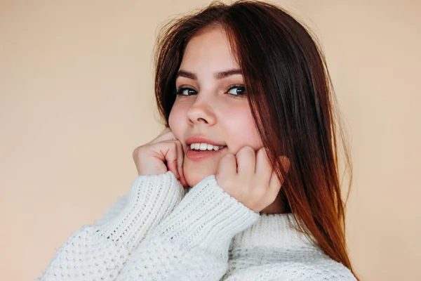 Portret van mooie lachende tiener meisje met schone huid en donker lang haar in gezellige witte trui op beige achtergrond — Stockfoto