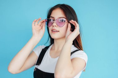 Mavi arka planda izole beyaz t-shirt koyu uzun saçlı kalp şekli güneş gözlüğü güzel kız