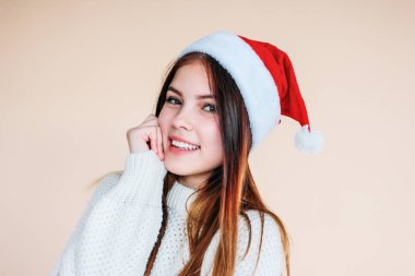 Santa şapka temiz cilt ile güzel gülümseyen kız bej arka planda rahat bir beyaz kazak