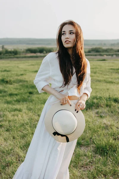 Bella spensierata capelli lunghi ragazza asiatica in vestiti bianchi e cappello di paglia gode la vita nel campo al tramonto. Sensibilità al concetto di natura — Foto Stock