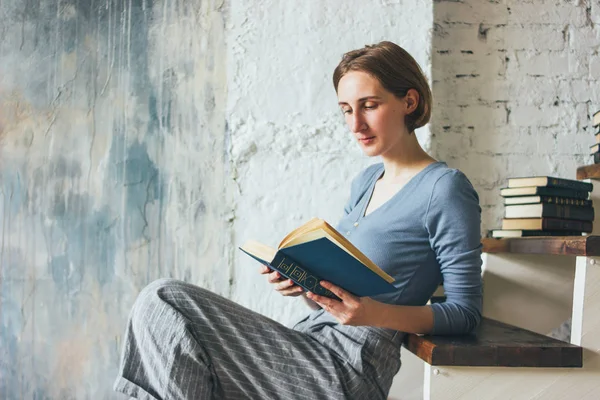 Young woman reading book on stairs in loft art work studio room, slow life — Stock Photo, Image