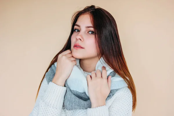 Mooi meisje met schone huid en donker lang haar in gezellige witte trui en warme sjaal op beige achtergrond — Stockfoto